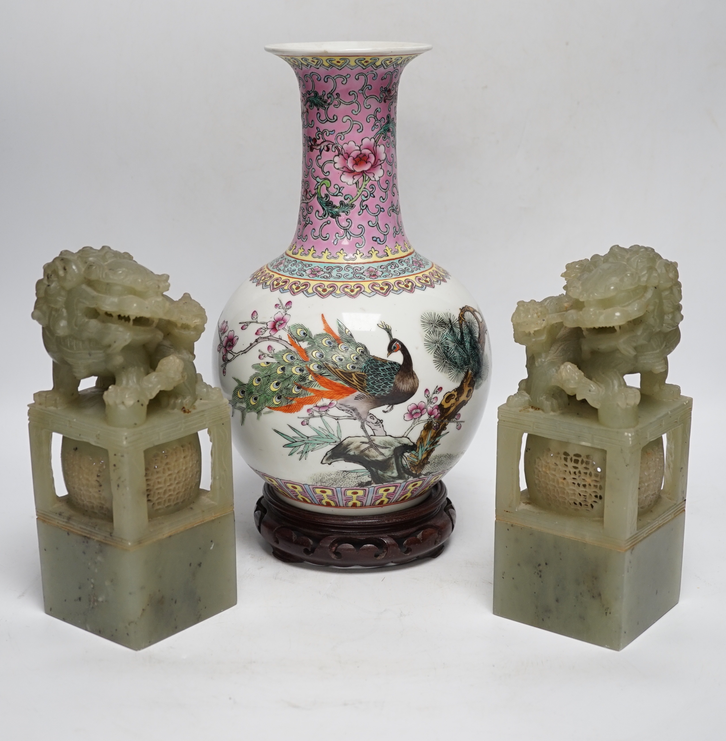 A pair of large Chinese soapstone ‘Temple Guardian lion’ seals, 21cm, and a Chinese famille rose vase, 27cm, on carved wood stand